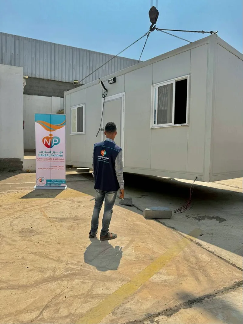 A Nahbal team member in front of a clinic unit suspended from lifting rigging, beside a company banner