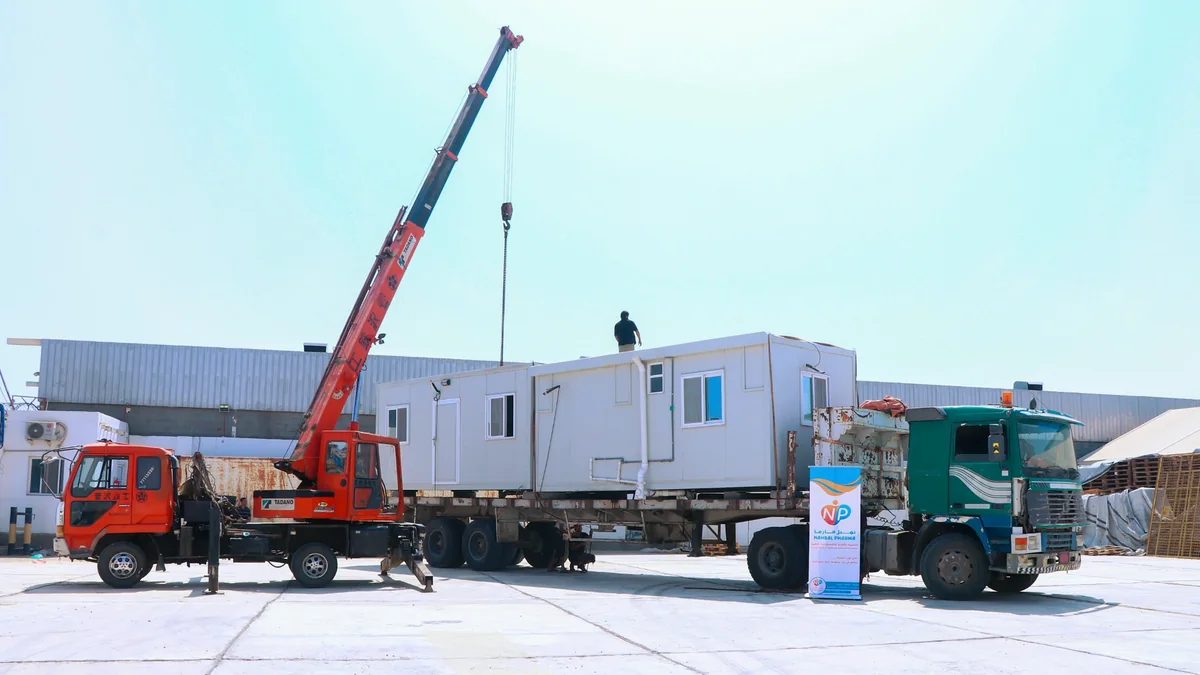 Mobile clinic units on a green truck beside a red crane and a Nahbal Pharma banner