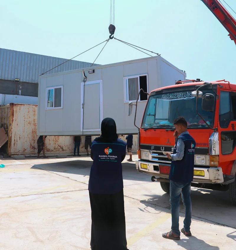A closer photograph of two Nahbal team members beside a clinic unit during handling, with company branding visible on their vests